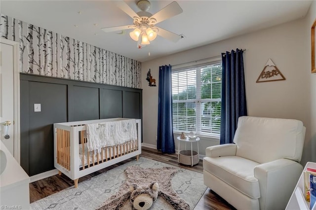 bedroom featuring a nursery area, wood finished floors, a ceiling fan, and baseboards