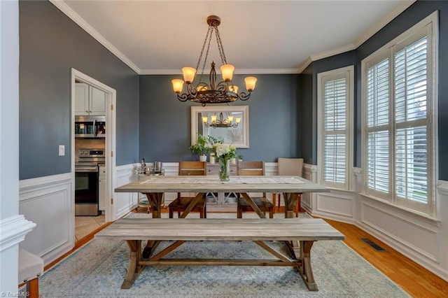 dining space featuring light wood-type flooring, a chandelier, healthy amount of natural light, crown molding, and wainscoting