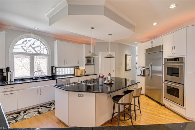 kitchen with a breakfast bar area, a sink, light wood-style floors, built in appliances, and a center island