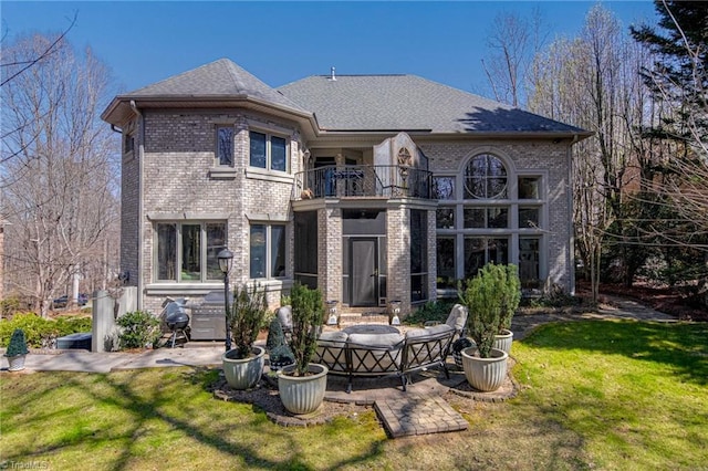 back of house featuring brick siding, a patio area, a yard, and a balcony