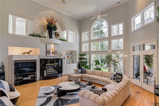 living area with a high end fireplace, french doors, a towering ceiling, wood finished floors, and a ceiling fan