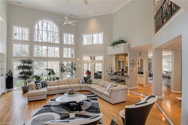 living room with light wood-style flooring, a ceiling fan, baseboards, and a towering ceiling