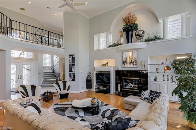 living room with ceiling fan, light wood-type flooring, a towering ceiling, and stairs