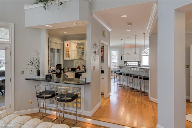 bar with ornamental molding, decorative light fixtures, wood finished floors, wet bar, and baseboards