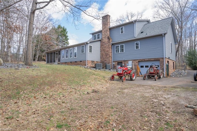 rear view of property with a sunroom, a yard, an attached garage, a shingled roof, and a chimney