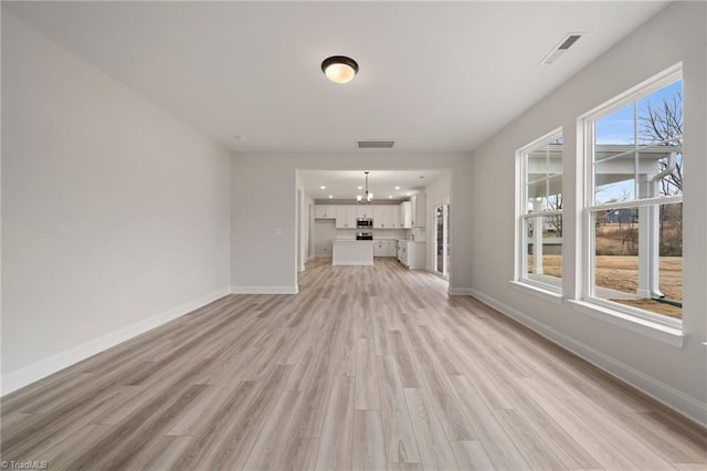 unfurnished living room featuring a notable chandelier and light hardwood / wood-style flooring