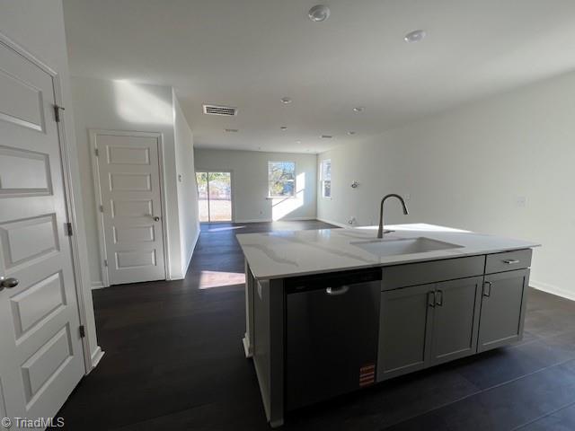 kitchen featuring sink, stainless steel dishwasher, gray cabinets, an island with sink, and light stone countertops