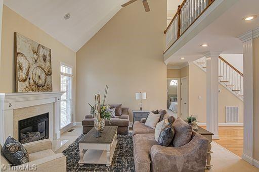 living room with light wood-type flooring, ceiling fan, a high end fireplace, and high vaulted ceiling