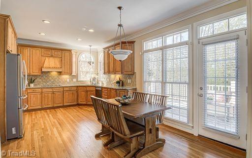 interior space featuring light hardwood / wood-style flooring, custom range hood, appliances with stainless steel finishes, crown molding, and hanging light fixtures