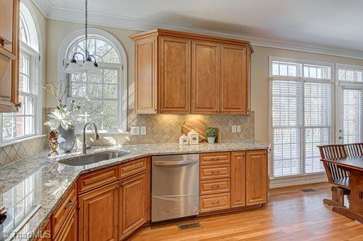 kitchen featuring light stone countertops, dishwasher, ornamental molding, and sink