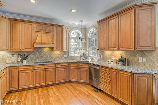 kitchen with backsplash, premium range hood, crown molding, stainless steel dishwasher, and light wood-type flooring