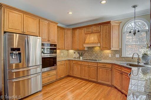 kitchen with appliances with stainless steel finishes, light stone countertops, sink, premium range hood, and ornamental molding