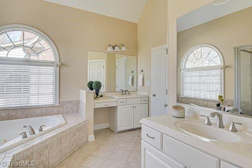 bathroom with tile patterned flooring, vanity, tiled bath, and high vaulted ceiling