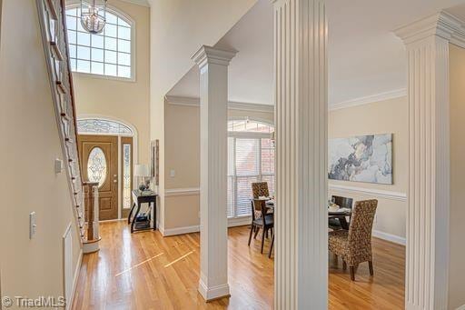 entryway with decorative columns, ornamental molding, an inviting chandelier, and light hardwood / wood-style flooring