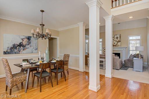 dining space featuring light wood-type flooring, ornamental molding, a chandelier, and ornate columns