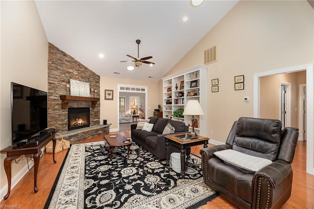 living room with a stone fireplace, ceiling fan, high vaulted ceiling, and light wood-type flooring