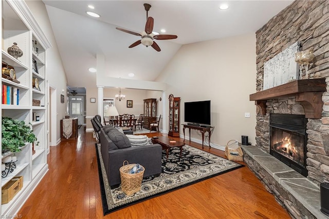 living room with ornate columns, ceiling fan, dark wood-type flooring, high vaulted ceiling, and a stone fireplace