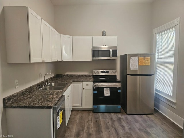 kitchen with dark wood-style flooring, appliances with stainless steel finishes, a sink, baseboards, and white cabinets