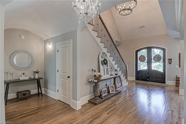 foyer with hardwood / wood-style floors, a notable chandelier, lofted ceiling, and french doors