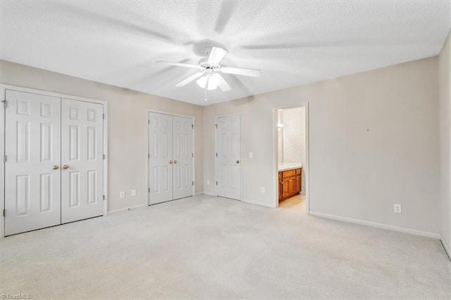 unfurnished bedroom with light carpet, ensuite bath, a textured ceiling, ceiling fan, and multiple closets