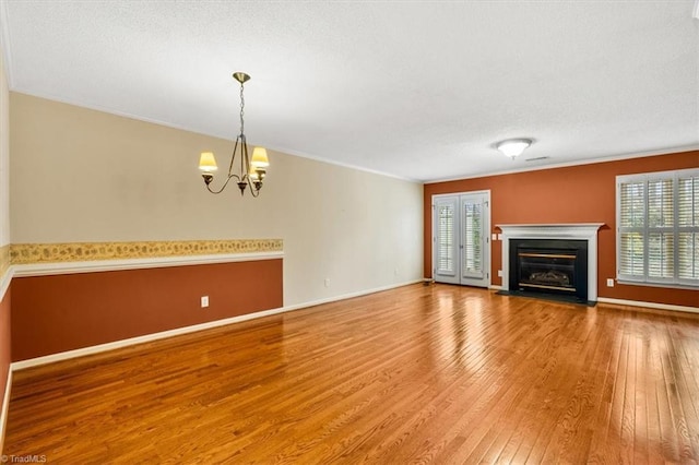 unfurnished living room with hardwood / wood-style flooring, ornamental molding, and an inviting chandelier