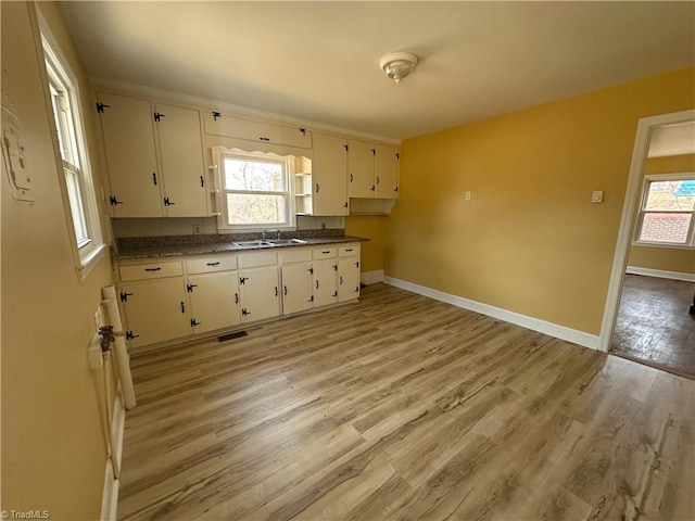 kitchen with a sink, visible vents, baseboards, light wood finished floors, and dark countertops