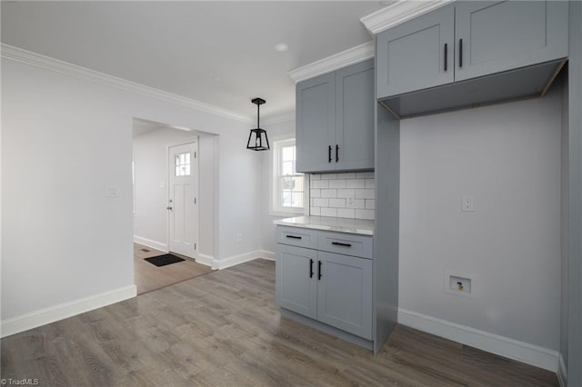 kitchen featuring gray cabinetry, hardwood / wood-style floors, tasteful backsplash, ornamental molding, and decorative light fixtures