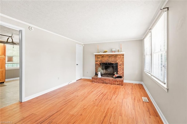 1765 K Fork Rd, Madison, NC 27025 - unfurnished living room featuring light wood-style flooring, a textured ceiling, a brick fireplace, ornamental molding, and baseboards