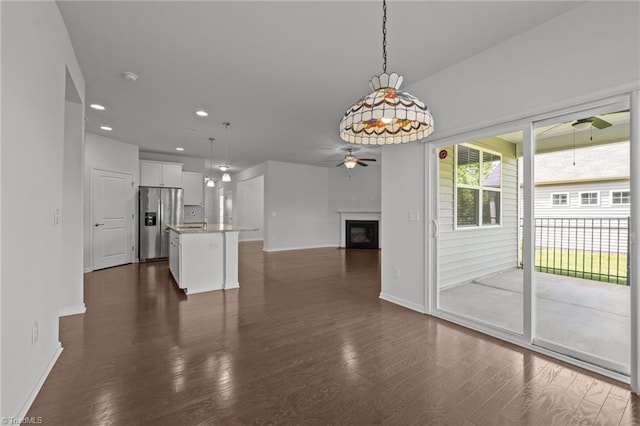 interior space featuring a glass covered fireplace, a ceiling fan, baseboards, and dark wood-type flooring