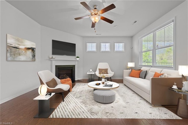living room with a fireplace with flush hearth, wood finished floors, visible vents, baseboards, and ceiling fan