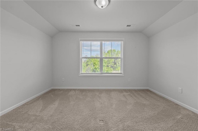 carpeted spare room with lofted ceiling, baseboards, and visible vents