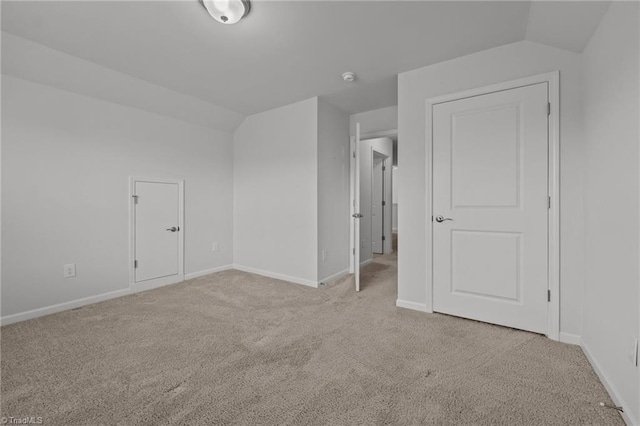 unfurnished bedroom featuring baseboards, lofted ceiling, and light colored carpet