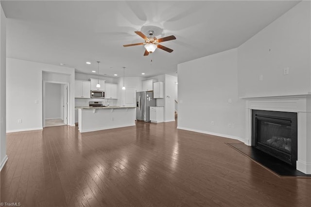 unfurnished living room with recessed lighting, a ceiling fan, dark wood-type flooring, baseboards, and a glass covered fireplace