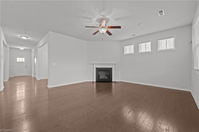 unfurnished living room with a ceiling fan, a fireplace with flush hearth, baseboards, dark wood-style flooring, and visible vents