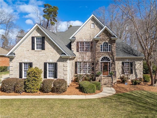 traditional-style house featuring stone siding, roof with shingles, a front lawn, and brick siding