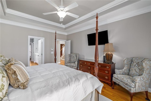 bedroom featuring ceiling fan, connected bathroom, wood finished floors, ornamental molding, and a tray ceiling