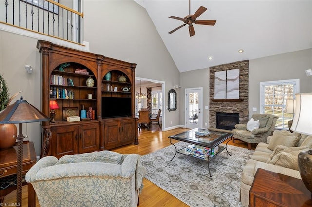 living area featuring light wood-style floors, a fireplace, high vaulted ceiling, and a ceiling fan