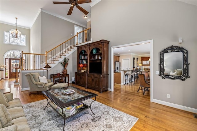 living area with light wood-style flooring, a towering ceiling, baseboards, ornamental molding, and stairway