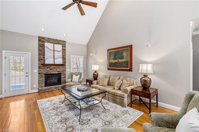 living area with high vaulted ceiling, a fireplace, light wood-style flooring, and baseboards