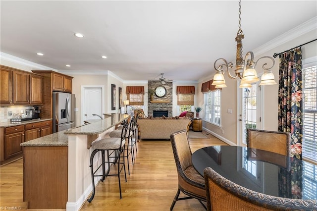 kitchen featuring light wood finished floors, brown cabinetry, stainless steel fridge with ice dispenser, a kitchen breakfast bar, and a fireplace