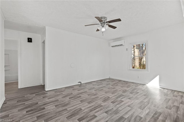 empty room featuring a wall mounted AC, a textured ceiling, light wood-type flooring, and ceiling fan