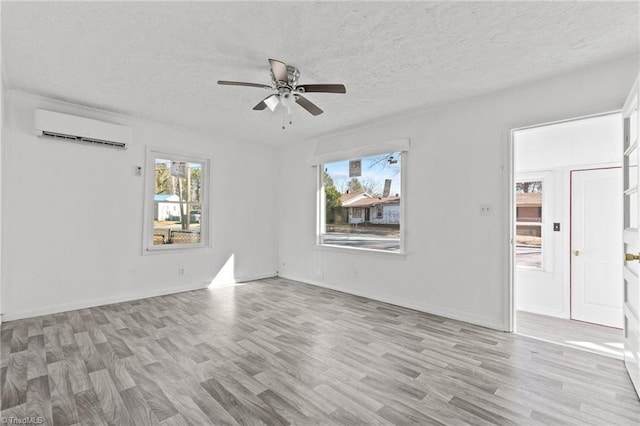 spare room with an AC wall unit, a textured ceiling, a wealth of natural light, and light hardwood / wood-style flooring