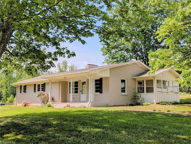 single story home with a porch, board and batten siding, a chimney, a front yard, and brick siding