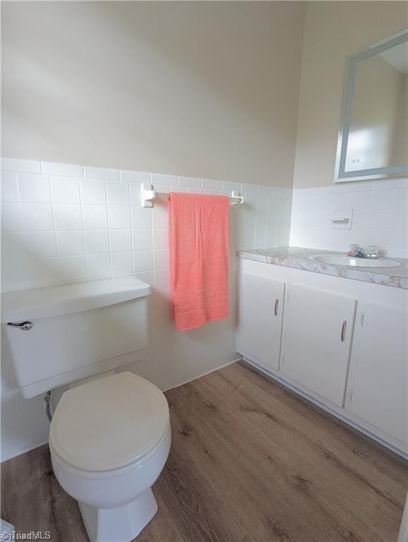 bathroom featuring tile walls, wood finished floors, a wainscoted wall, vanity, and toilet