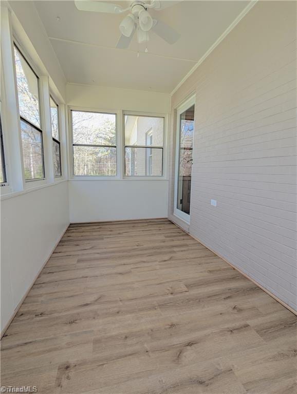 unfurnished sunroom with brick wall, ceiling fan, and wood finished floors