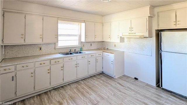 kitchen featuring freestanding refrigerator, under cabinet range hood, decorative backsplash, and a sink