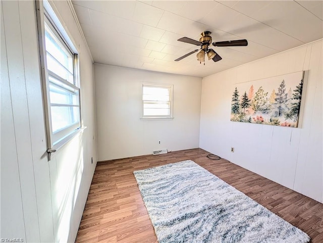 unfurnished room with a ceiling fan, wood walls, visible vents, and light wood-type flooring