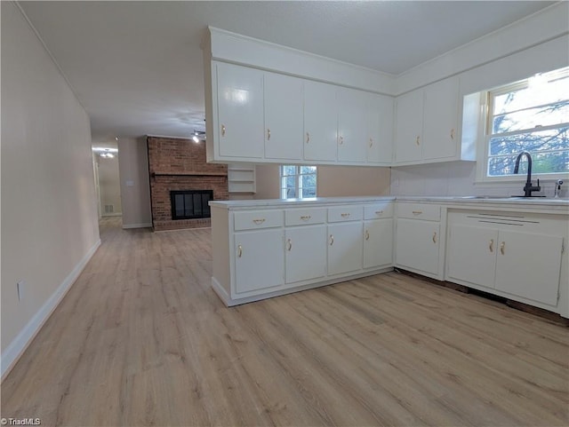 kitchen with white cabinets, a sink, a fireplace, light countertops, and light wood-style floors