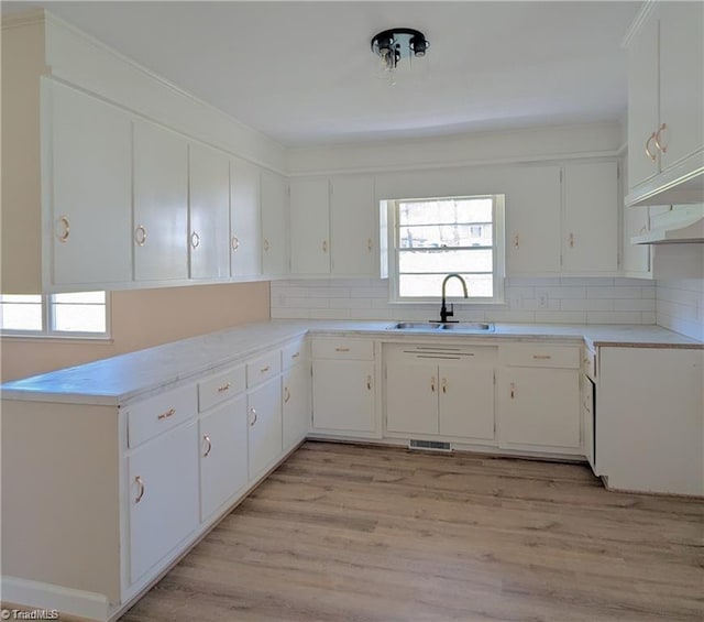 kitchen with a sink, light countertops, decorative backsplash, light wood-type flooring, and visible vents