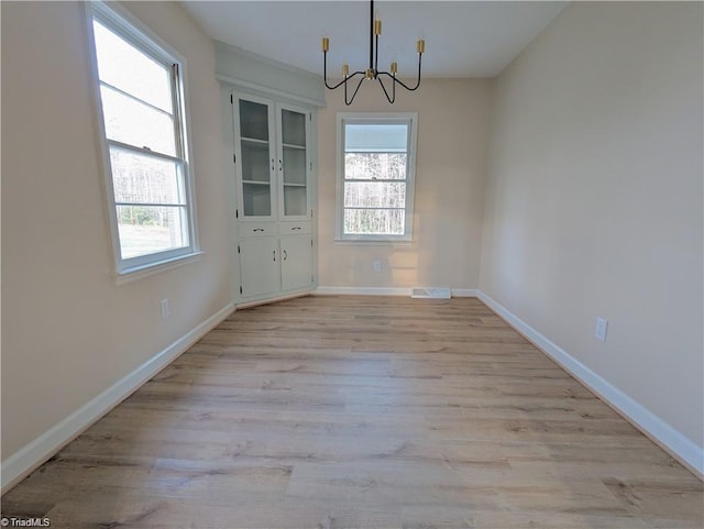 unfurnished dining area featuring an inviting chandelier, baseboards, plenty of natural light, and light wood-style flooring